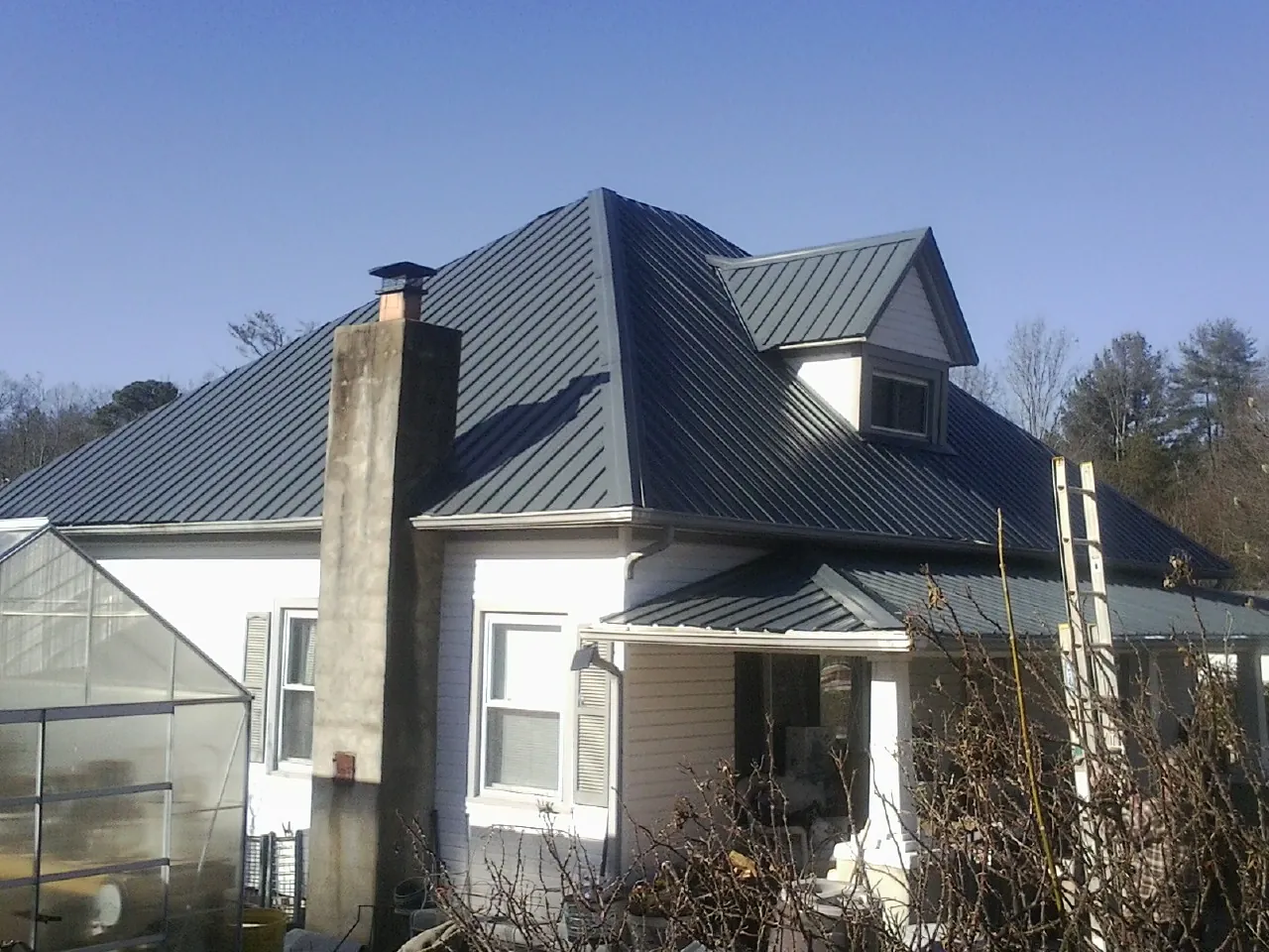 Dark blue standing seam metal roof on a white farmhouse with dormer — Slate & Tile Roof Repair by Roofing Brothers in Pickrell