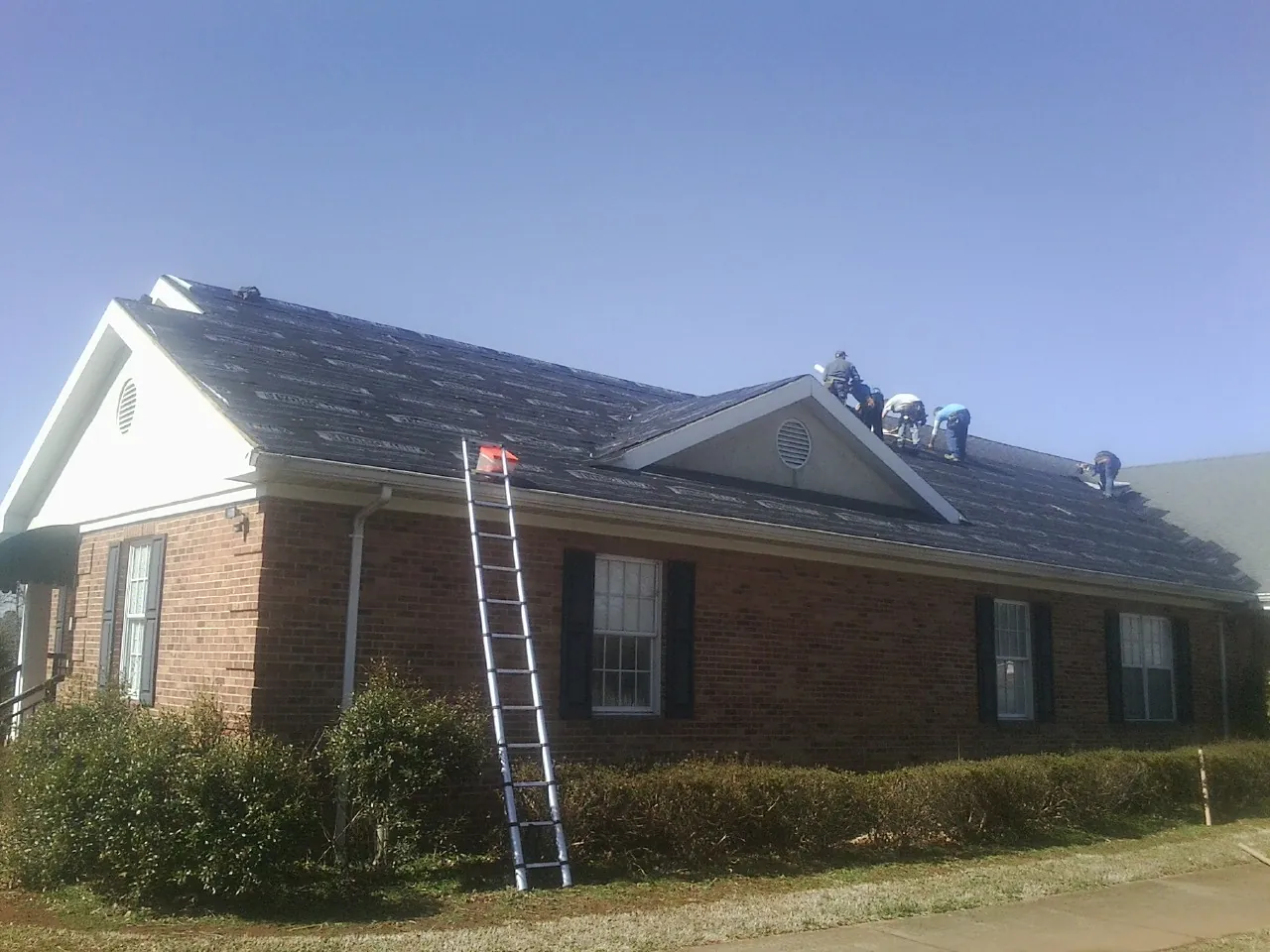 Crew tearing shingles off a brick ranch roof with a ladder set — Emergency Roof Repair work by our crew in Pickrell