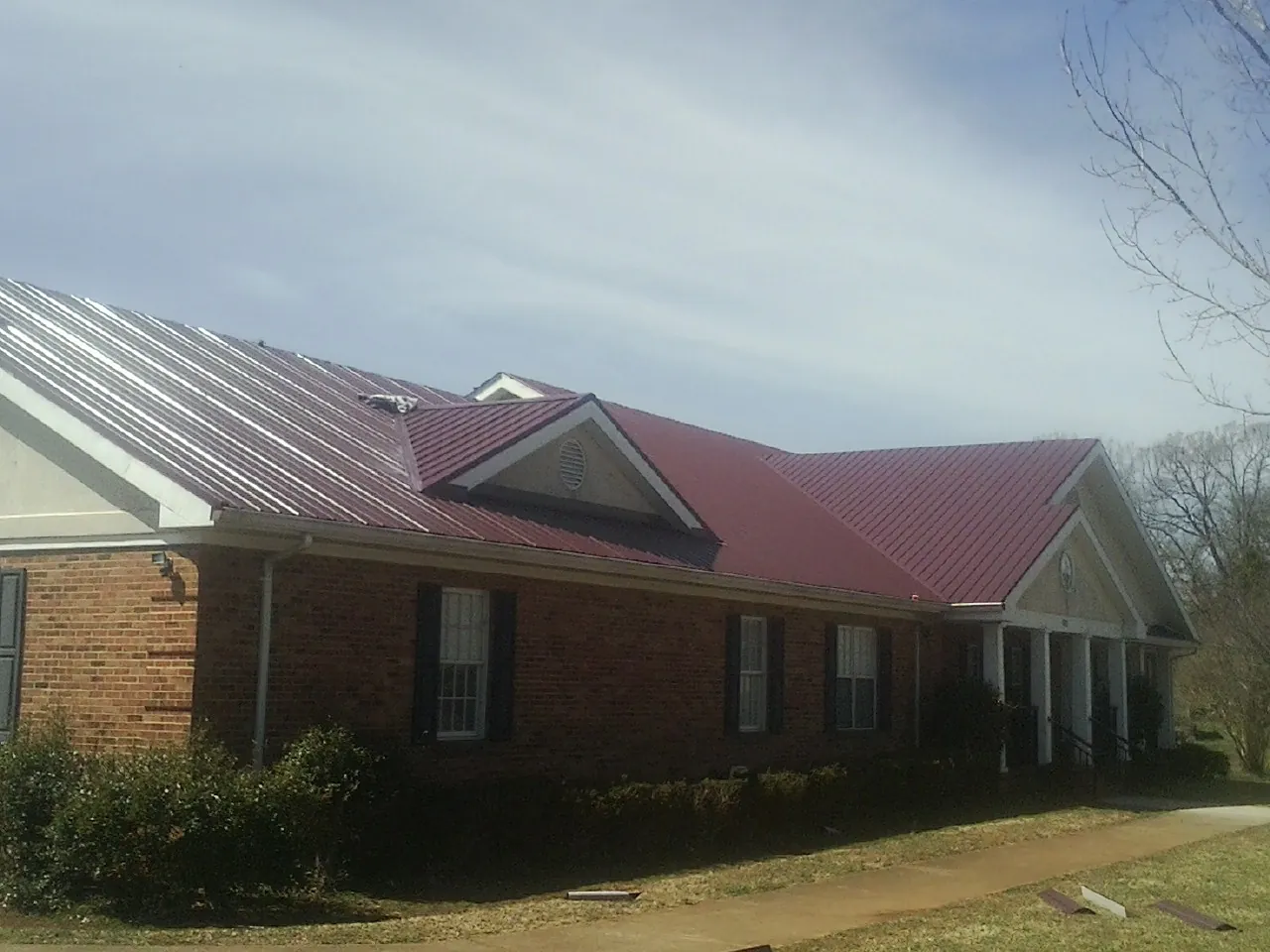 Red metal roof with gabled entries on a long brick building, from a Hail Damage Roof Repair job in Pickrell
