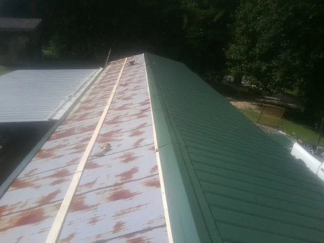 Old rusted panels beside newly installed green metal roofing — Wind Damage Roof Repair by Roofing Brothers in Pickrell