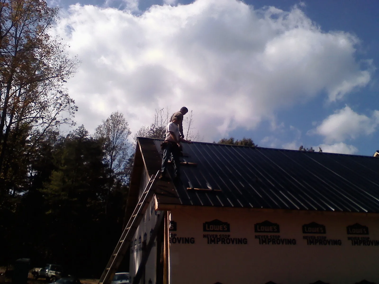Roofer fastening dark metal panels high against a cloudy sky, from a Roof Inspection job in Pickrell